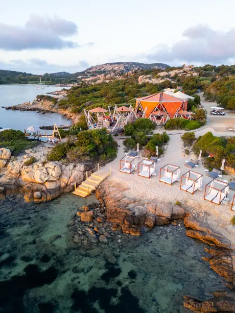 Seaside view of a beach restaurant with cabanas and rocky shores.