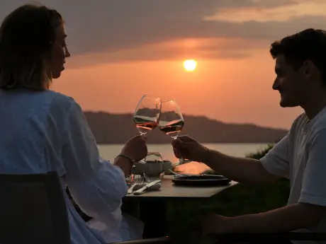 Couple toasting wine glasses against a stunning sunset backdrop.