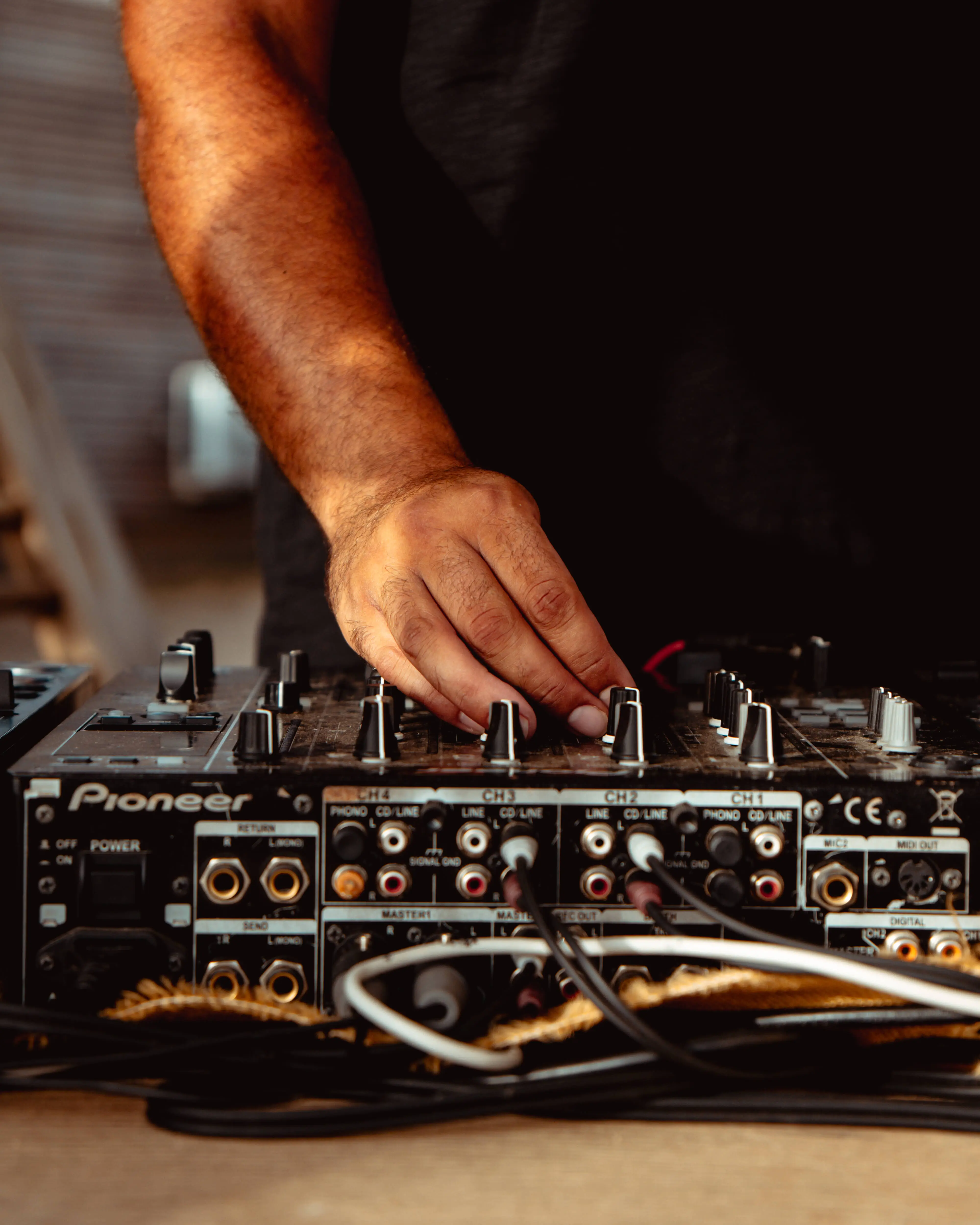 DJ's hand on Pioneer mixer with audio cables.