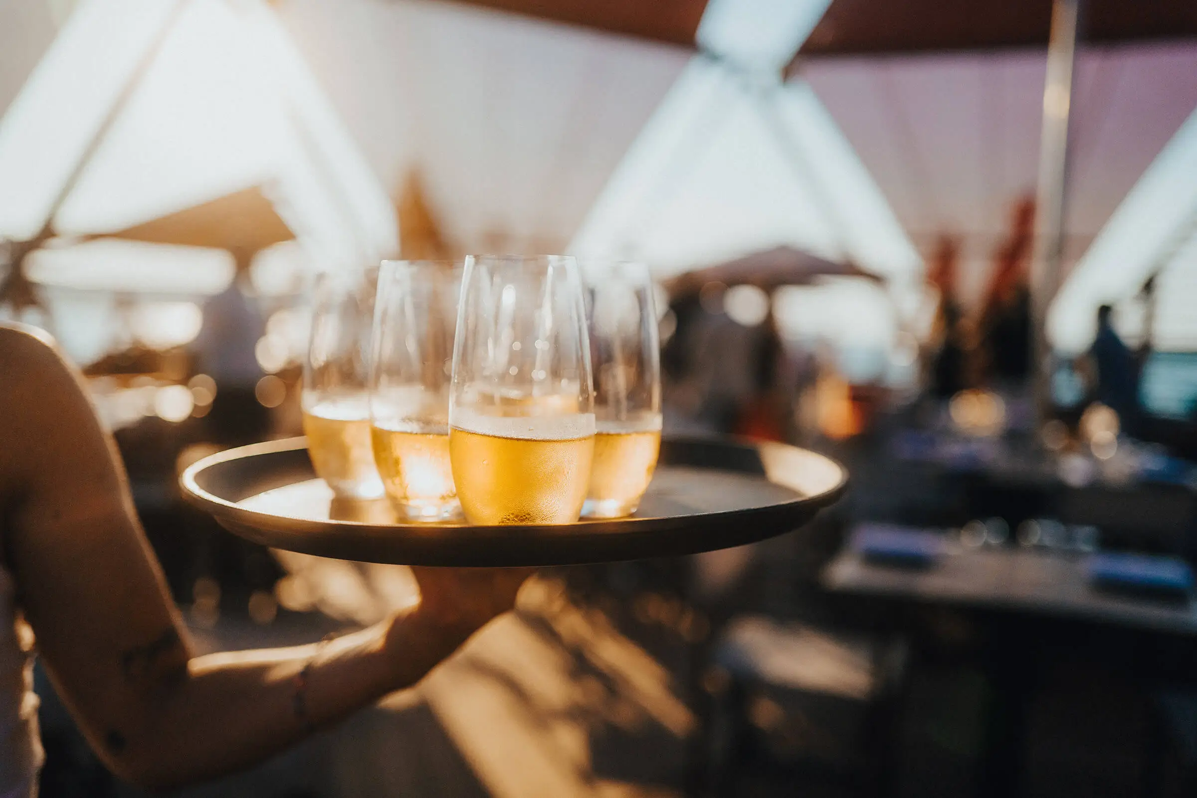 Waiter serving beer glasses on a tray at an outdoor seaside restaurant during aperitif service.