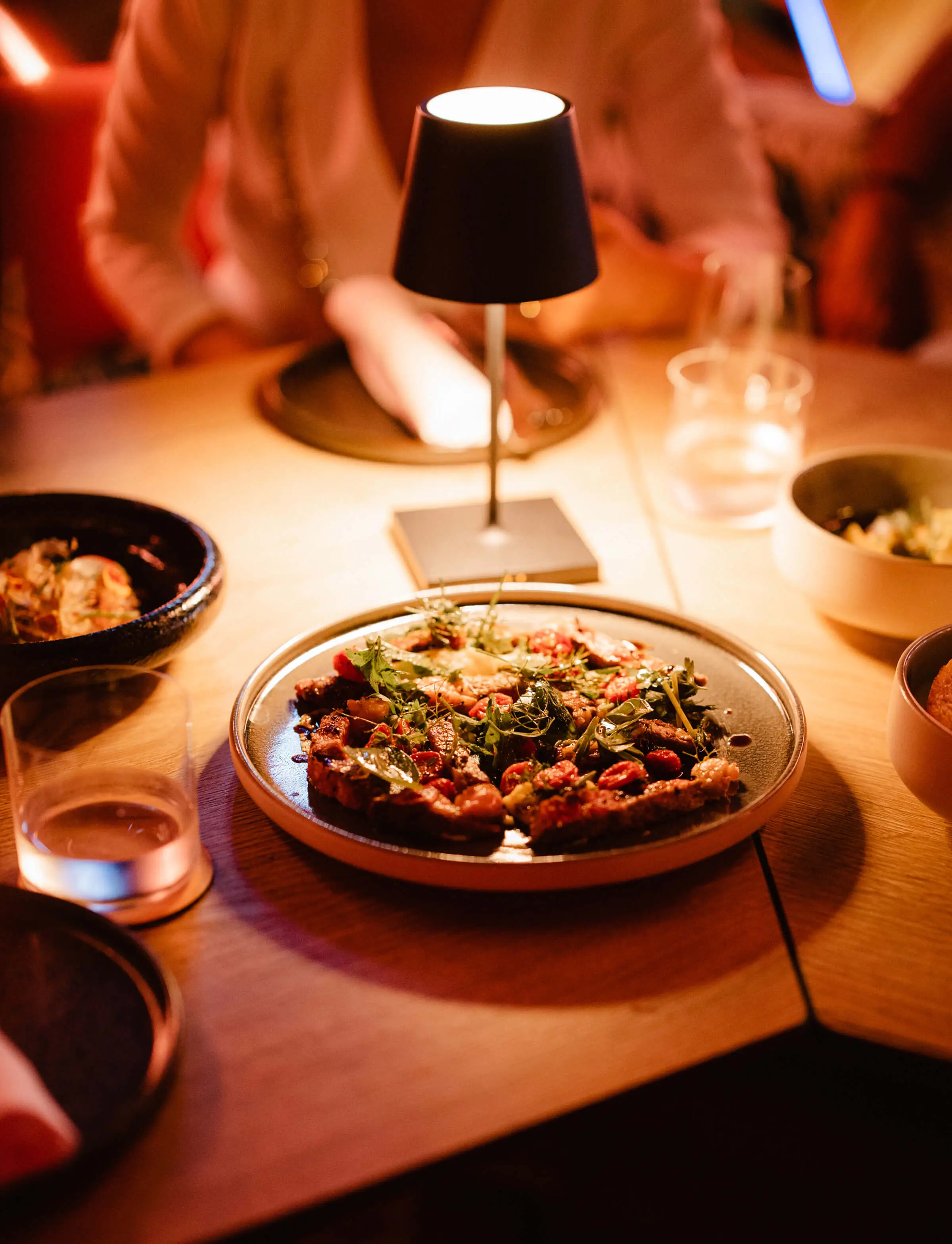 Warmly lit restaurant table with a gourmet plated dish under a small lamp.
