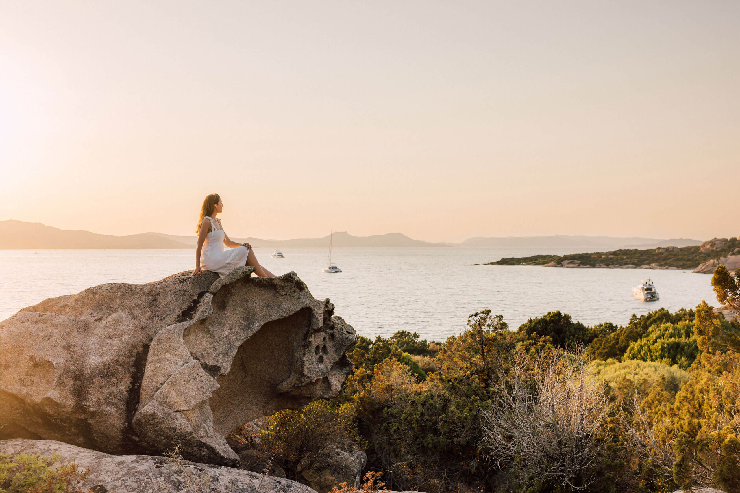 A woman sitting on a rock overlooking a body of water