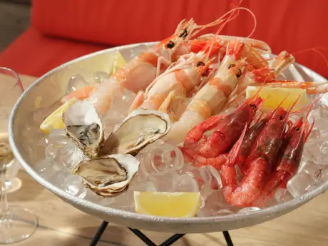 Fresh seafood platter with prawns, oysters, and lemon slices on ice.