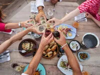 Un gruppo di persone che godono dell'esperienza di cucina in riva al mare di Tohru Nakamura con piatti caratteristici e bicchieri di vino