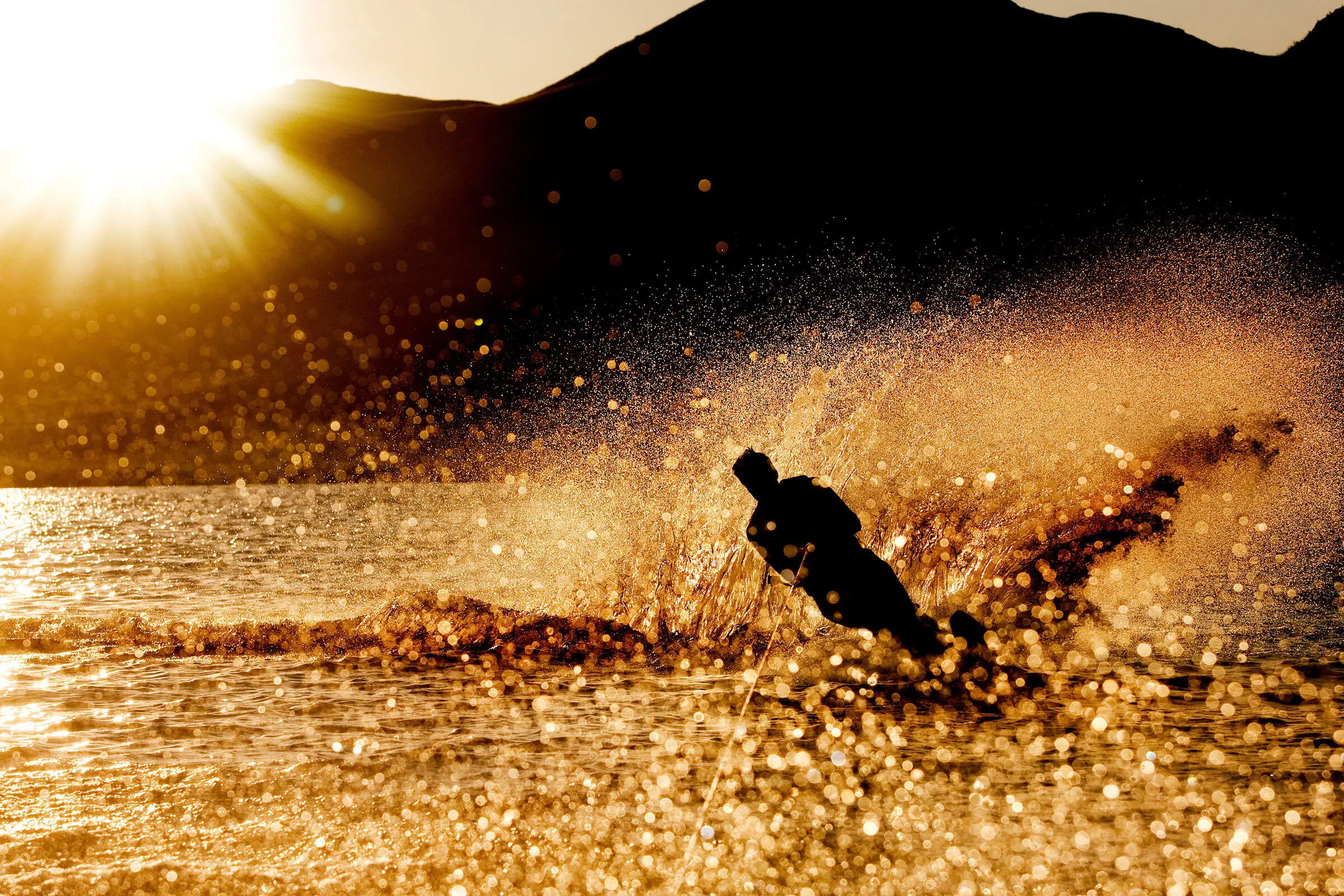 A water skier carving across a lake at sunset, throwing up a dramatic golden spray.